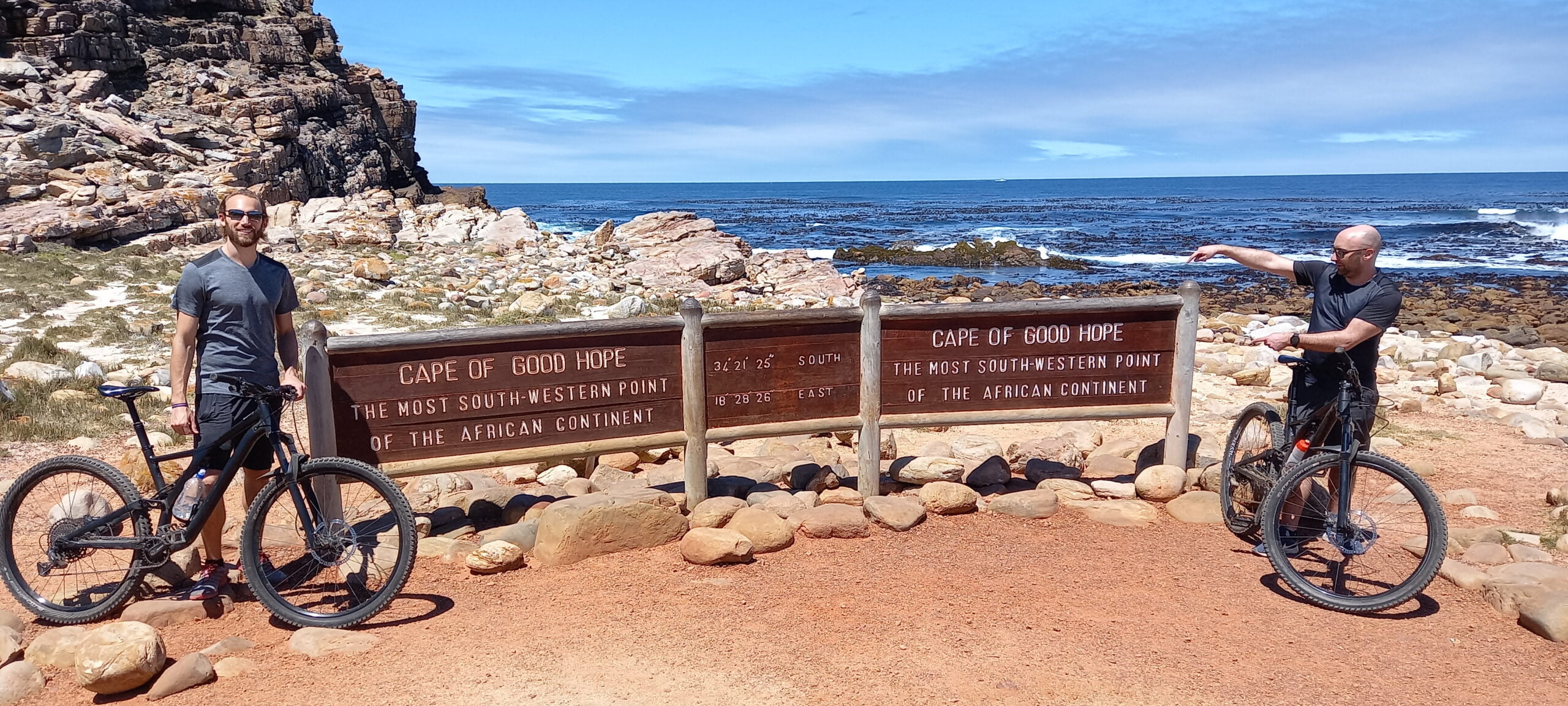 Two cyclists with mountain bikes enjoying a scenic coastal stop during a Cape Peninsula cycling tour.