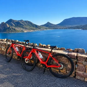 Two red road bicycles at a scenic viewpoint overlooking a blue bay and rugged mountains on the Cape Peninsula near Cape Town.